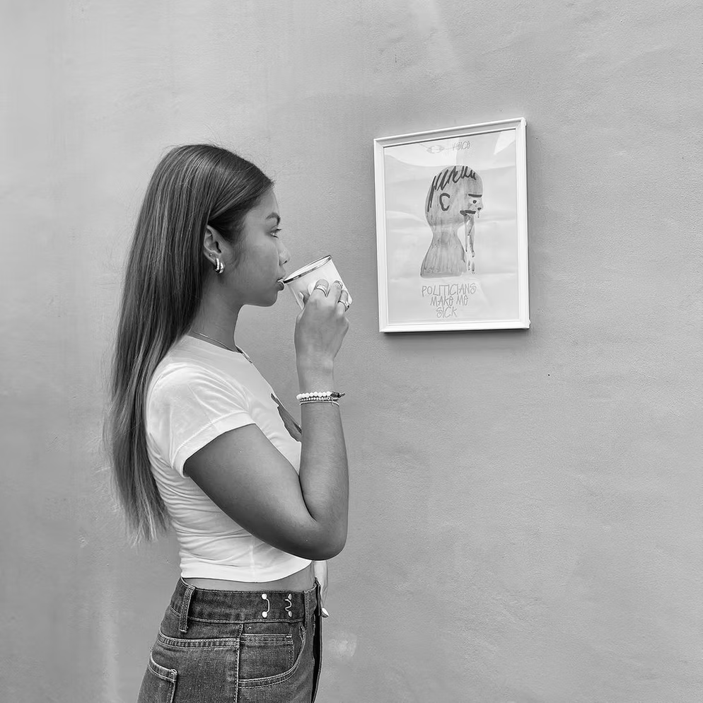 Woman drinking from a Herblunt Mug in front of a framed picture on a gray wall