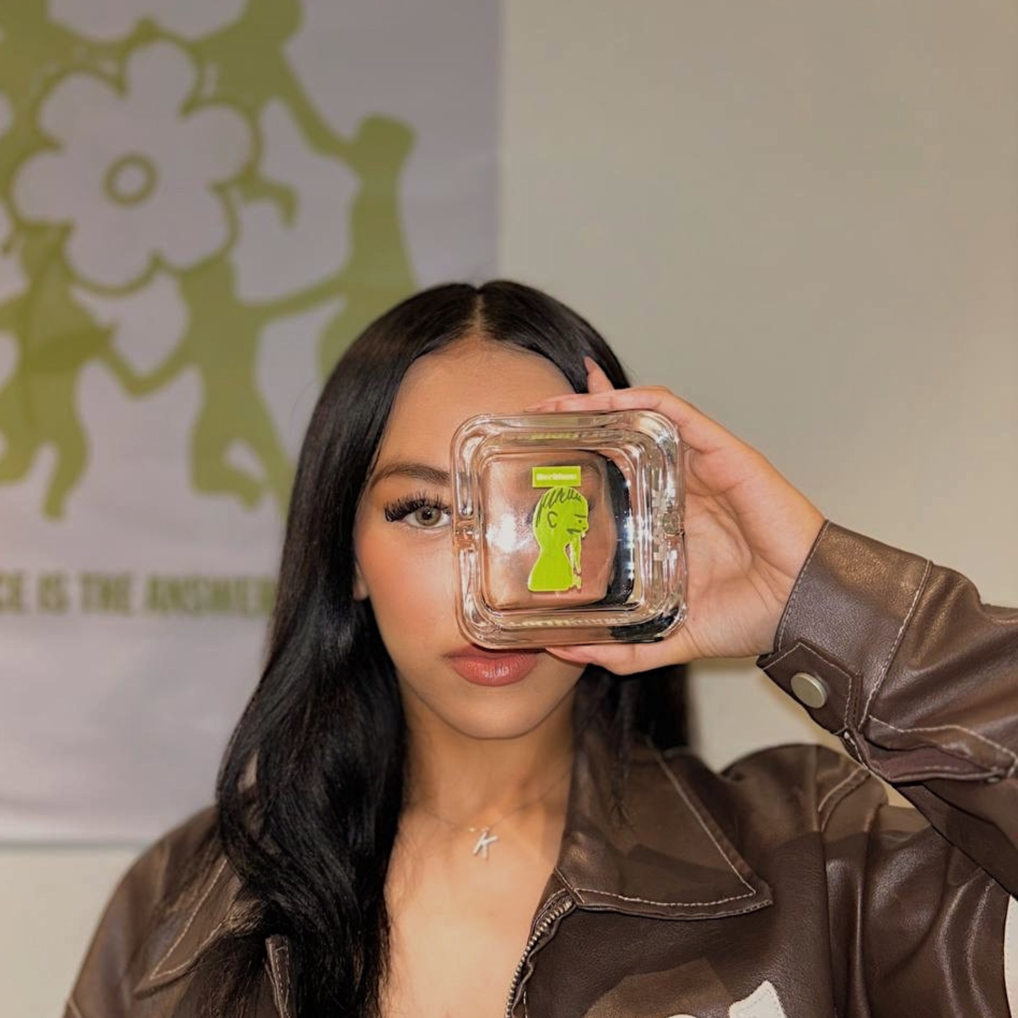 Person holding a herblunt ashtray with a design on it, wearing a brown jacket.